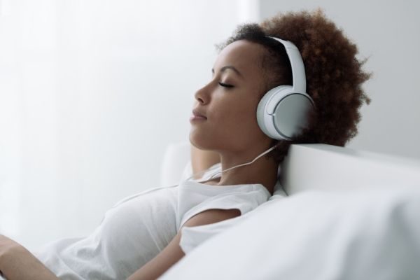 woman listening on headphones to positive input as part of her daily self care checklist printable