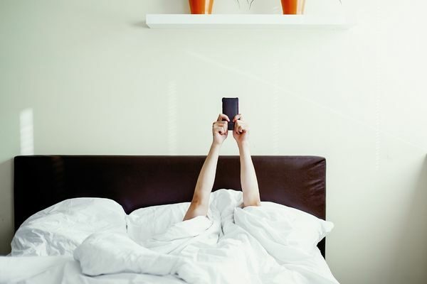 holding cell phone in bed; detox social media challenge cleanse