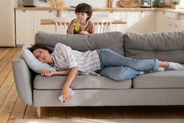 mom laying on couch with child standing behind her: mommy burnout