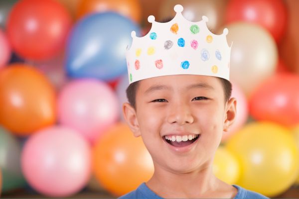 boy smiling with crown and balloons