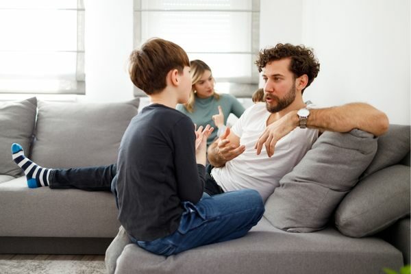two adults and two kids talking on a couch