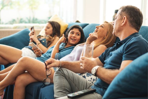 family sitting on a couch watching tv; spring break staycation ideas