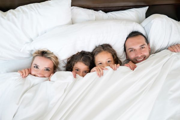 family of four in a bed with covers pulled up; spring break staycation ideas, summer, winter
