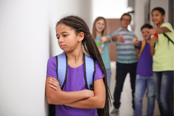 girl standing in the hallway sad with other students pointing at her