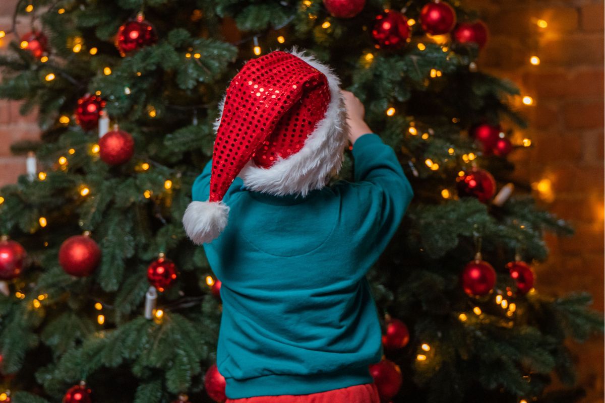child in santa hat hanging an ornament on tree
